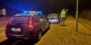noc, na zdjęciu samochód służbowy Straży Granicznej a przed nim kontrolowany pojazd, obok stoi umundurowany funkcjonariusz Straży Granicznej
