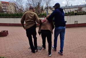 Zatrzymani za przyrzut ludzi przez granicę Dwóch funkcjonariuszy Straży Granicznej w ubraniach cywilnych prowadzi między sobą mężczyznę, który ma założone na ręce z tyłu kajdanki