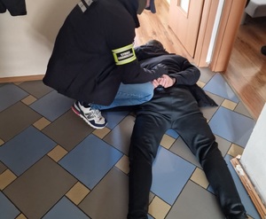 Zatrzymani za przyrzut ludzi przez granicę Funkcjonariusz Straży Granicznej klęczy obok leżącego na brzuchu na podłodze skutego kajdankami mężczyzny