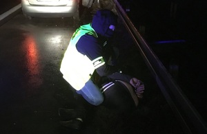 Zatrzymani za przyrzut ludzi przez granicę Funkcjonariusz Straży Granicznej klęczy obok leżącego na ziemi, zatrzymanego mężczyzny.