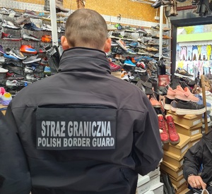Funkcjonariusz Straży Granicznej podczas kontroli stoiska z podrobioną odzieżą Funkcjonariusze Straży Granicznej podczas kontroli stoiska z podrobioną odzieżą