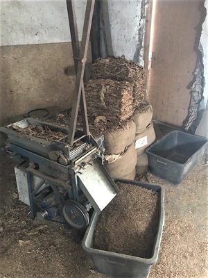 Zabezpieczona krajalnica do tytoniu krajalnica do tytoniu stoi na podłodze garażu, obok czarne murarskie pojemniki służące jako pojemniki do tytoniu