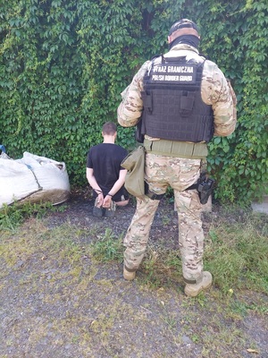Zatrzymany do sprawy mężczyzna Zatrzymany do sprawy mężczyzna klęczy a obok stoi umundurowany funckjoanriusz Straży Granicznej